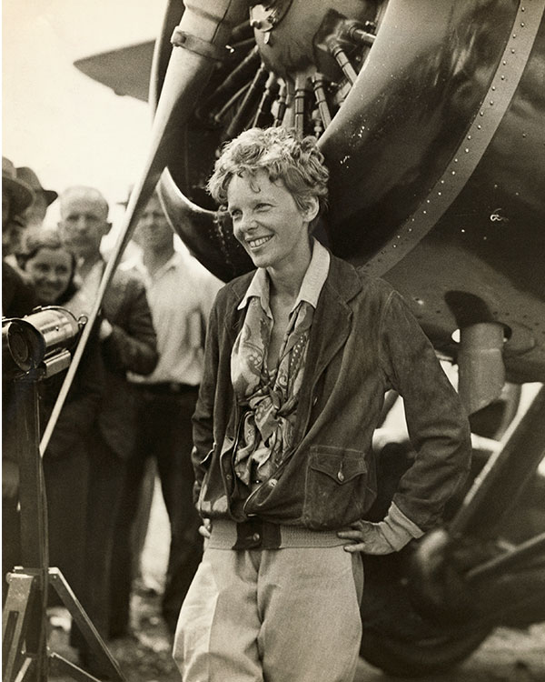 Amelia Earhart smiles and poses with her plane.