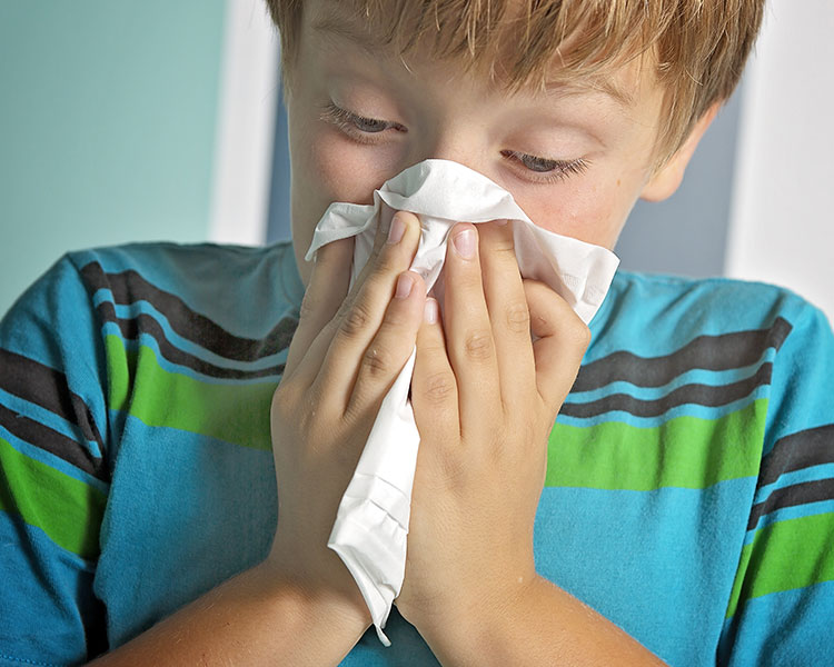 A young boy sneezes into a tissue paper.