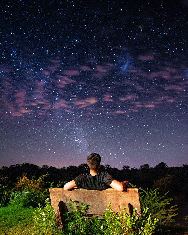 A boy sits on a bench while watching the night sky.