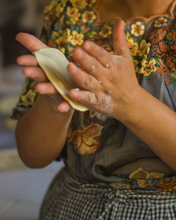 A woman flattens a corn tortilla with her hands.