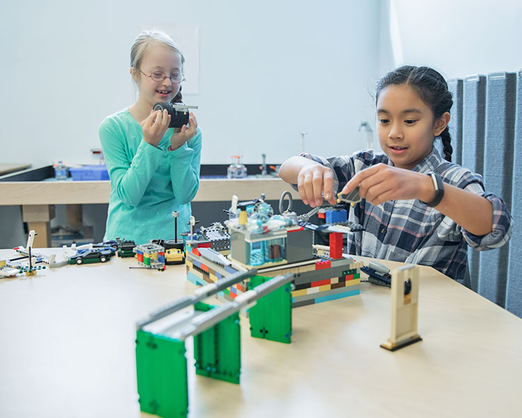 Two young girls build a mechanized Lego set.