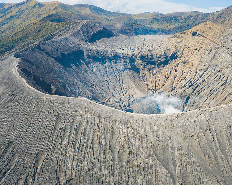 A large smoking caldera is round with a deep pit in the center.