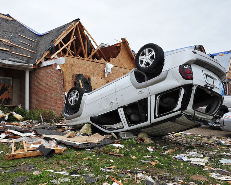 An upside-down car in front of a damaged house.