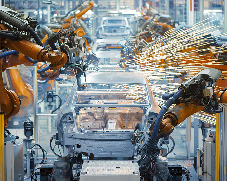 Robotic arms assemble cars on an assembly line.