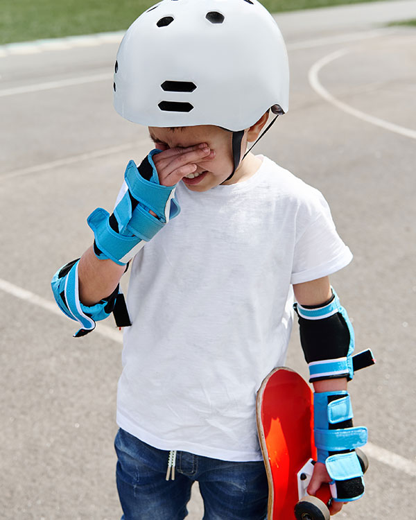 young boy wearing skateboarding gear and looking upset