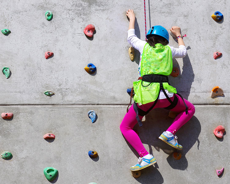 child climbing a rock-climbing wall in a safety harness