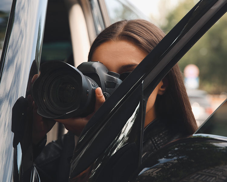 A woman hiding herself and her camera between her car door sneakily taking a picture