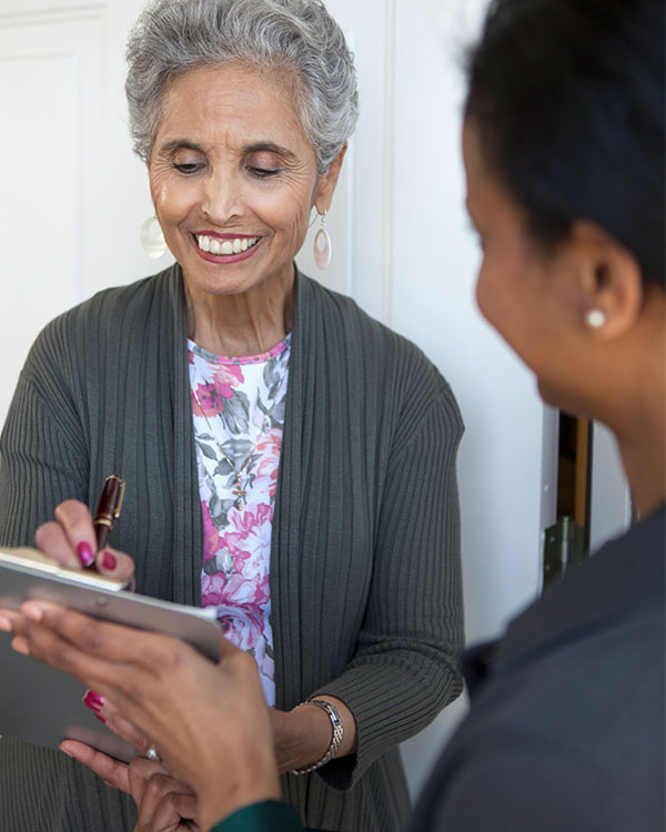 Photo of a smiling person signing a clipboard that another person is holding