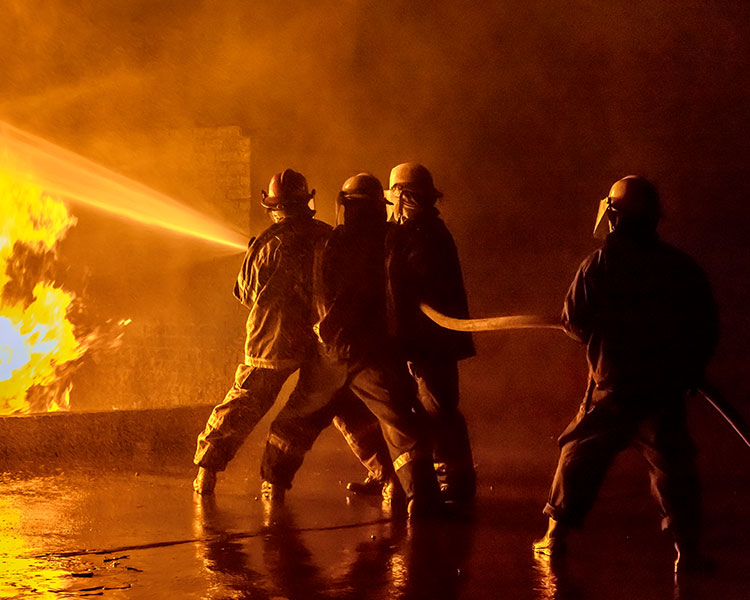 Four firefighters using a hose to put out a large fire