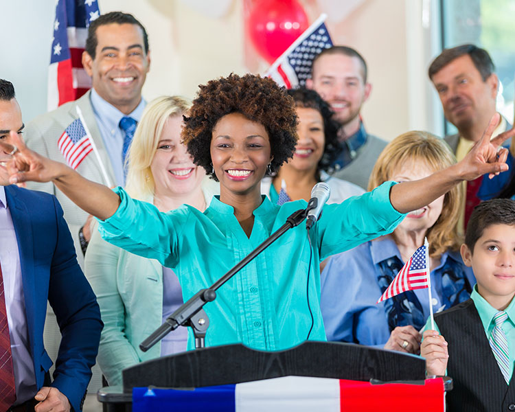 Photo of a political candidate standing at podium with supporters in background