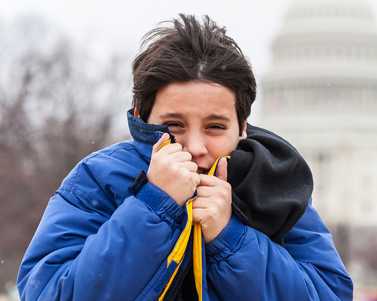 Photo of a shivering kid bringing his jacket closer to his face to shield the cold